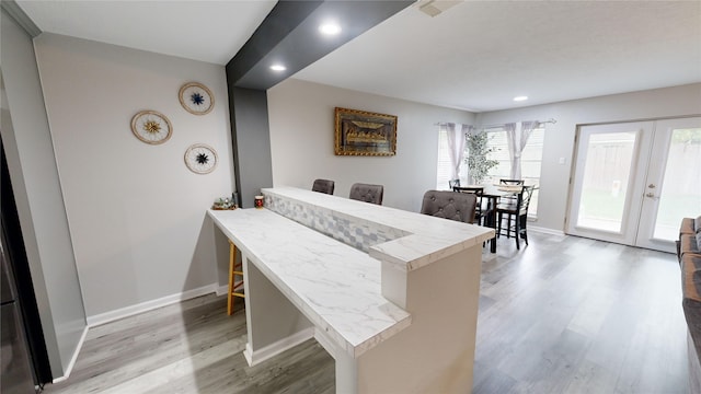 kitchen with kitchen peninsula, a breakfast bar, french doors, and light hardwood / wood-style flooring