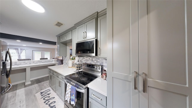 kitchen featuring light wood-type flooring, stainless steel appliances, tasteful backsplash, and gray cabinetry