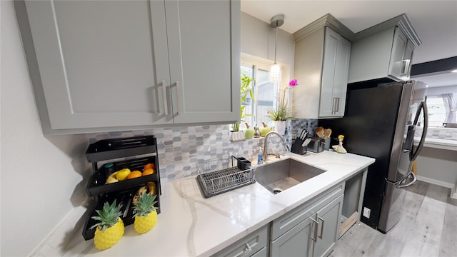 kitchen with light stone countertops, sink, gray cabinets, stainless steel refrigerator, and hanging light fixtures