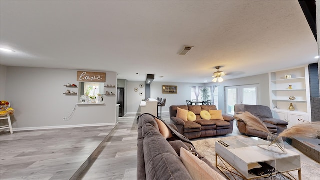 living room with built in shelves, ceiling fan, wood-type flooring, and a textured ceiling