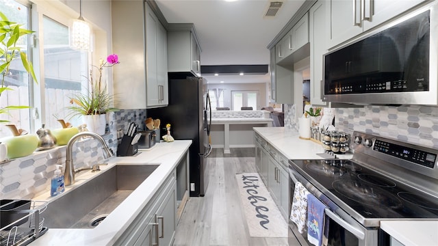 kitchen with sink, decorative light fixtures, gray cabinets, appliances with stainless steel finishes, and light wood-type flooring