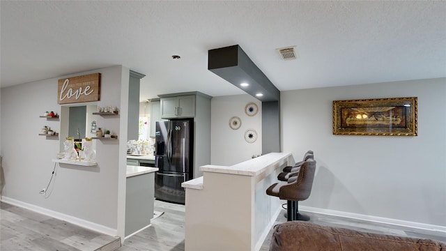 kitchen featuring a kitchen breakfast bar, kitchen peninsula, stainless steel fridge, a textured ceiling, and light wood-type flooring