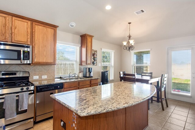 kitchen featuring stainless steel appliances, sink, decorative light fixtures, a chandelier, and a center island