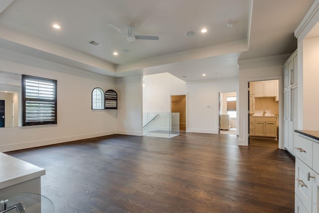 unfurnished living room featuring a raised ceiling, ceiling fan, dark hardwood / wood-style floors, and ornamental molding