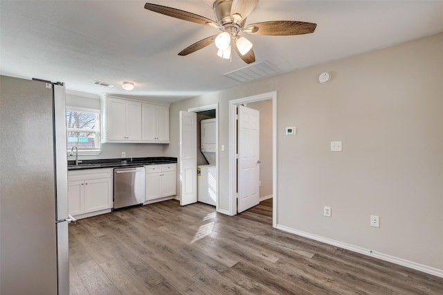 kitchen featuring white cabinets, sink, stacked washing maching and dryer, wood-type flooring, and stainless steel appliances