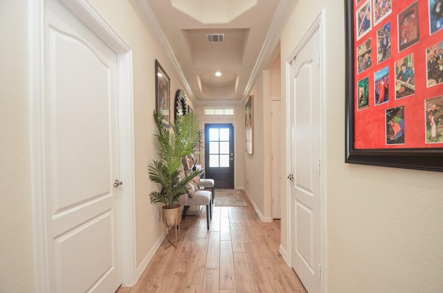 corridor with a raised ceiling, crown molding, and light hardwood / wood-style flooring