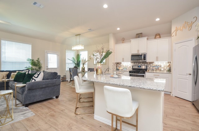 kitchen featuring decorative light fixtures, stainless steel appliances, white cabinetry, and an island with sink