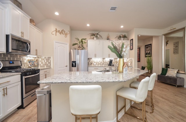 kitchen featuring white cabinetry, stainless steel appliances, a breakfast bar area, and an island with sink