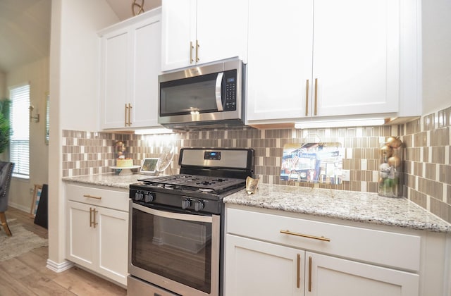 kitchen with white cabinets, light wood-type flooring, appliances with stainless steel finishes, tasteful backsplash, and light stone counters