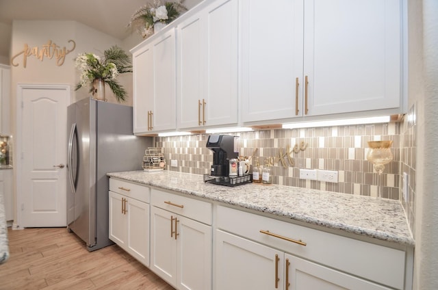 kitchen featuring white cabinets, light stone countertops, stainless steel refrigerator, and tasteful backsplash