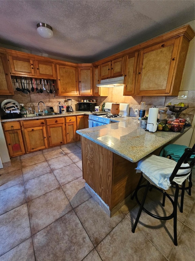 kitchen featuring a breakfast bar, sink, light stone counters, kitchen peninsula, and white range with gas cooktop