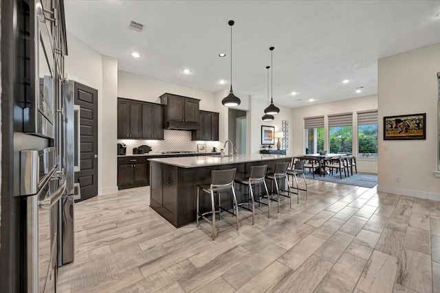 kitchen featuring sink, hanging light fixtures, an island with sink, a kitchen bar, and dark brown cabinets