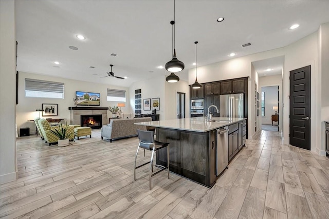 kitchen featuring hanging light fixtures, light hardwood / wood-style flooring, dark brown cabinets, a fireplace, and a center island with sink