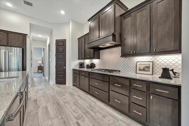 kitchen with dark brown cabinetry, light stone counters, light hardwood / wood-style flooring, and appliances with stainless steel finishes