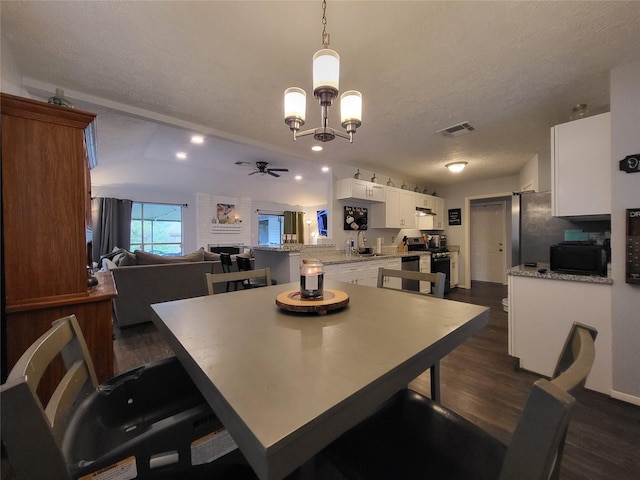 dining room with dark hardwood / wood-style flooring, ceiling fan with notable chandelier, a textured ceiling, vaulted ceiling, and sink