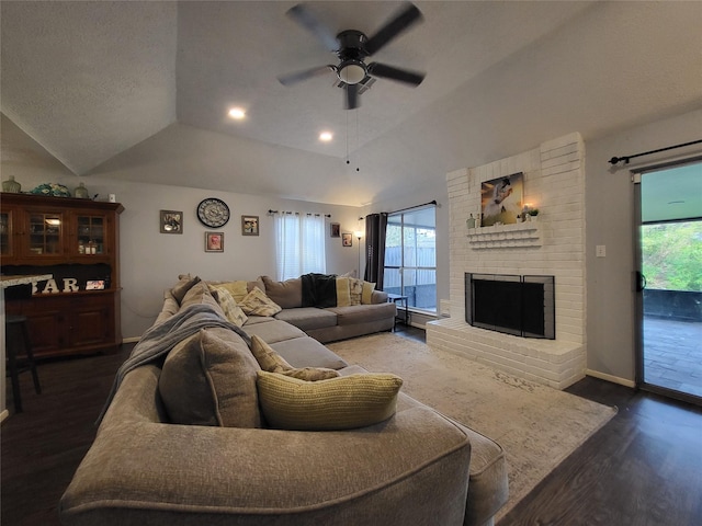 living room with ceiling fan, dark wood-type flooring, a brick fireplace, a textured ceiling, and lofted ceiling