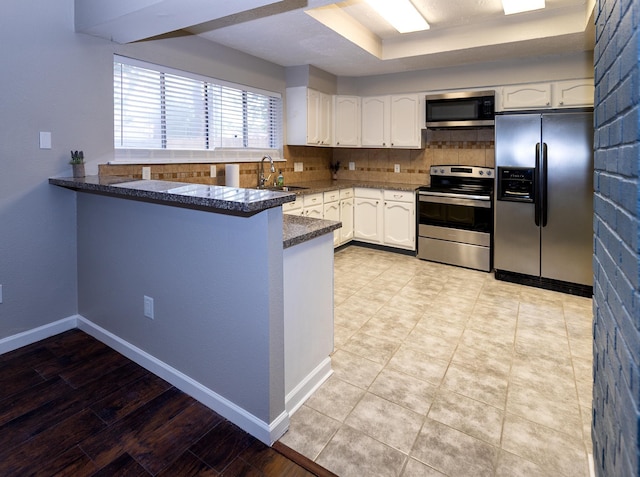 kitchen with kitchen peninsula, tasteful backsplash, stainless steel appliances, sink, and white cabinetry