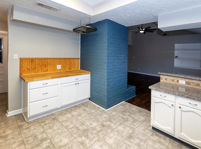 kitchen featuring a textured ceiling, ceiling fan, dark stone countertops, white cabinetry, and wood walls