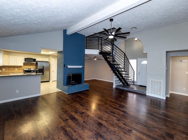 unfurnished living room with ceiling fan, a brick fireplace, vaulted ceiling with beams, hardwood / wood-style floors, and a textured ceiling