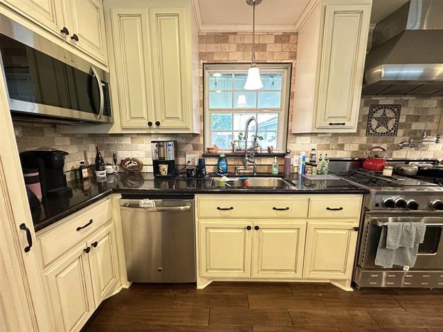 kitchen featuring ornamental molding, wall chimney exhaust hood, stainless steel appliances, sink, and decorative light fixtures