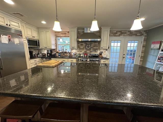 kitchen with french doors, wall chimney exhaust hood, decorative light fixtures, and appliances with stainless steel finishes