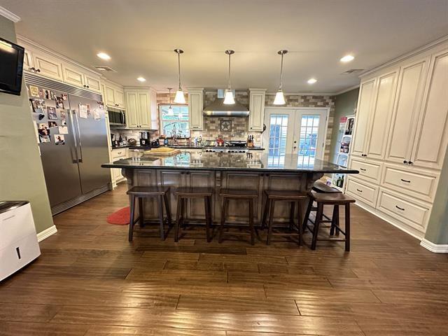 kitchen with wall chimney range hood, hanging light fixtures, appliances with stainless steel finishes, a kitchen island, and a breakfast bar area