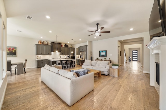 living room featuring ceiling fan, a premium fireplace, and light wood-type flooring