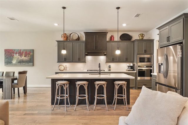 kitchen featuring decorative light fixtures, an island with sink, backsplash, and stainless steel appliances