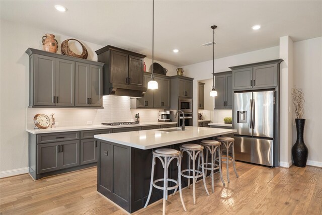 kitchen with stainless steel appliances, an island with sink, sink, hanging light fixtures, and a breakfast bar