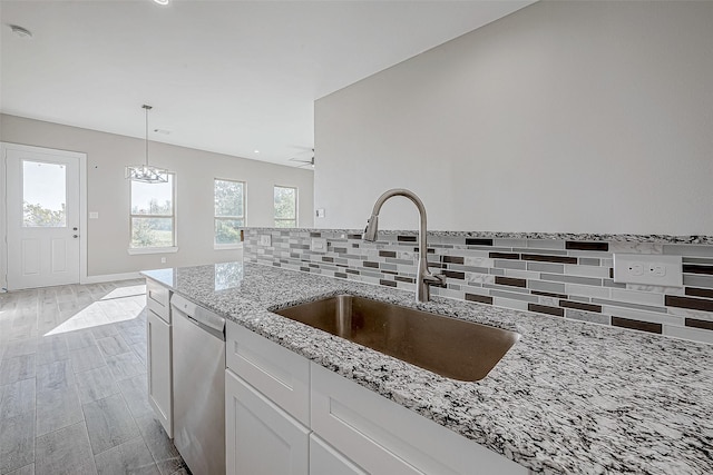 kitchen featuring dishwasher, sink, decorative backsplash, light stone counters, and white cabinetry