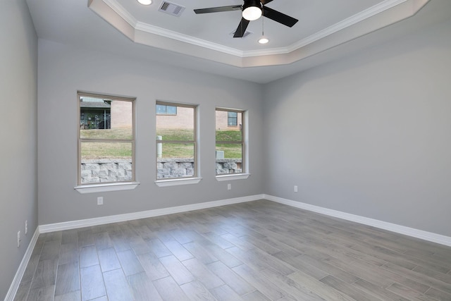 empty room with a raised ceiling, crown molding, ceiling fan, and light wood-type flooring