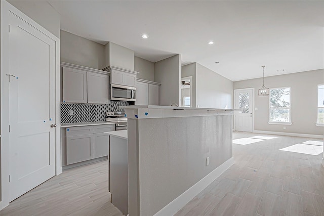 kitchen with gray cabinetry, pendant lighting, a center island with sink, appliances with stainless steel finishes, and tasteful backsplash