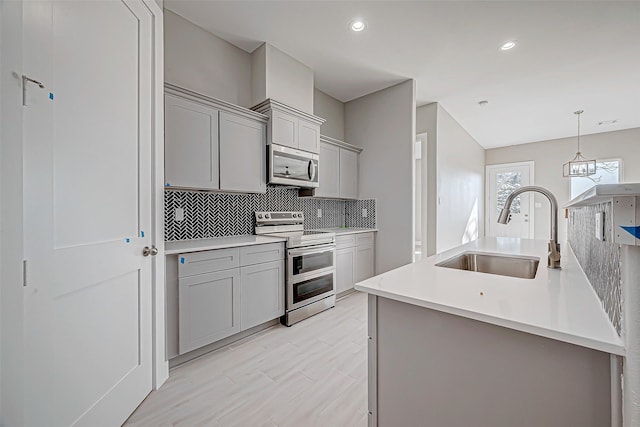 kitchen with sink, stainless steel appliances, backsplash, decorative light fixtures, and gray cabinets