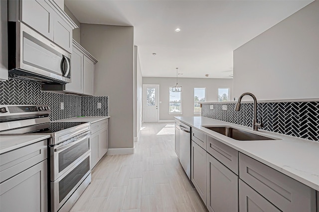 kitchen featuring gray cabinetry, sink, appliances with stainless steel finishes, decorative light fixtures, and light stone counters