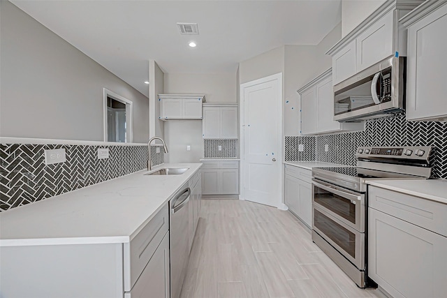 kitchen featuring decorative backsplash, appliances with stainless steel finishes, light wood-type flooring, and sink