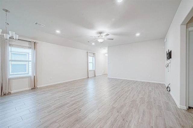 empty room featuring light wood-style flooring, recessed lighting, ceiling fan with notable chandelier, visible vents, and baseboards