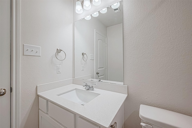 bathroom with toilet, a textured wall, visible vents, and vanity