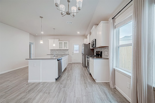 kitchen featuring a center island with sink, white cabinets, glass insert cabinets, appliances with stainless steel finishes, and decorative light fixtures