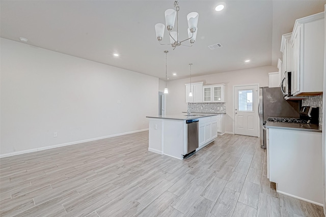 kitchen with a center island with sink, white cabinets, decorative backsplash, appliances with stainless steel finishes, and hanging light fixtures