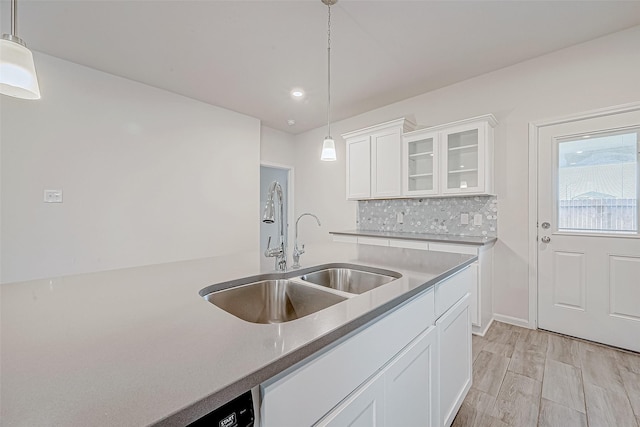 kitchen featuring decorative backsplash, white cabinets, glass insert cabinets, hanging light fixtures, and a sink