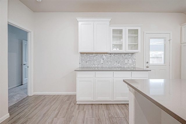 kitchen featuring light wood finished floors, decorative backsplash, glass insert cabinets, light countertops, and white cabinetry