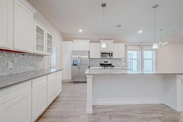 kitchen with white cabinets, stainless steel appliances, glass insert cabinets, and decorative light fixtures