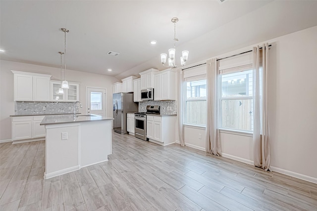 kitchen with appliances with stainless steel finishes, light countertops, hanging light fixtures, and a center island with sink