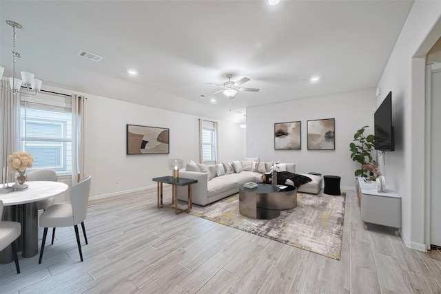 living area featuring light wood-style flooring, visible vents, baseboards, and ceiling fan with notable chandelier