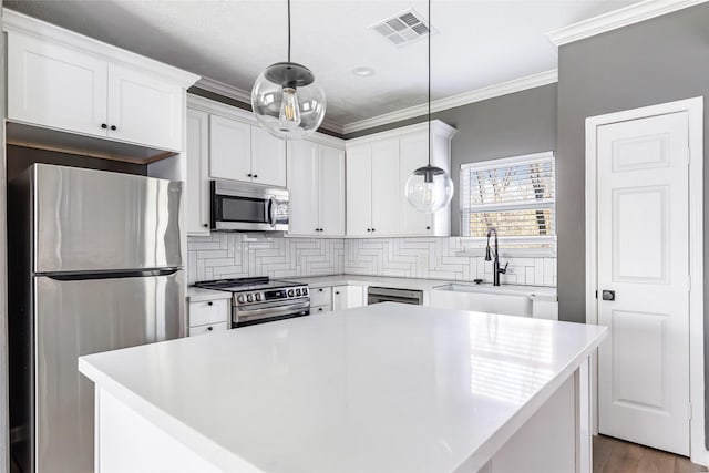 kitchen with appliances with stainless steel finishes, tasteful backsplash, pendant lighting, a center island, and white cabinetry