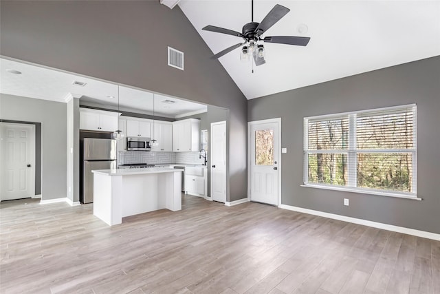 kitchen with tasteful backsplash, stainless steel appliances, a kitchen island, beam ceiling, and white cabinetry