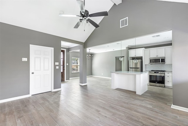 kitchen with white cabinets, hanging light fixtures, decorative backsplash, appliances with stainless steel finishes, and a kitchen island