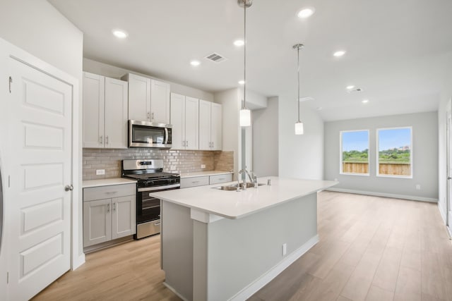 kitchen featuring sink, tasteful backsplash, an island with sink, pendant lighting, and stainless steel appliances