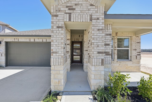 doorway to property with driveway, a shingled roof, an attached garage, and stone siding