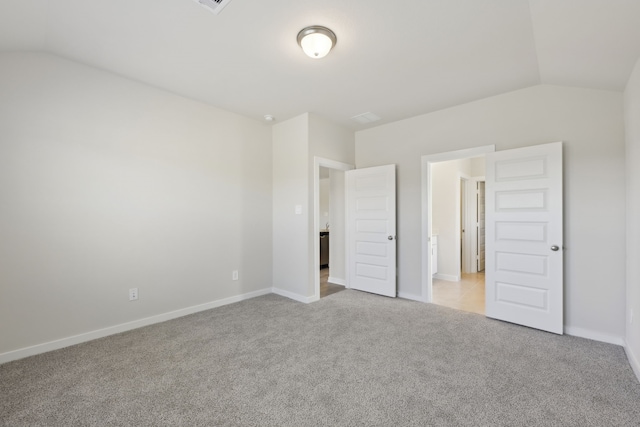 unfurnished bedroom featuring light carpet, vaulted ceiling, and baseboards